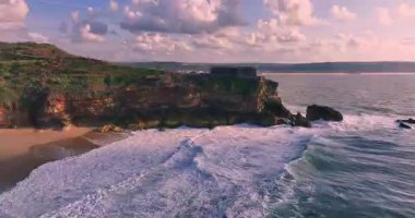 Güneş batarken kayalık bir kıyıya çarpan derin mavi okyanus dalgalarının dramatik hava manzarası bu sakin tropikal deniz manzarasını güzelleştirir. Seyahat, tatil ve doğa temaları için mükemmeldir..