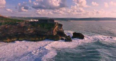 Güneş batarken kayalık bir kıyıya çarpan derin mavi okyanus dalgalarının dramatik hava manzarası bu sakin tropikal deniz manzarasını güzelleştirir. Seyahat, tatil ve doğa temaları için mükemmeldir..