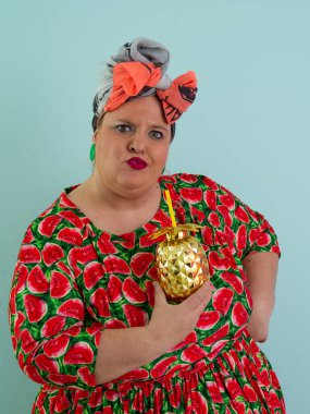 Karpuz desenli bir elbise giymiş tuhaf bir kadın ve elinde altın ananas şeklindeki bir kupayla kırmızı güneş gözlüklerinin üzerinden neşeyle bakan bir kupa tutuyor.. 