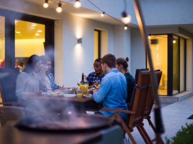 Bir grup genç insan akşamları modern bir evin terasında yemek yiyorlar. Dostlar ve aile için eğlence. Tatil kutlamaları, barbekülü düğünler..