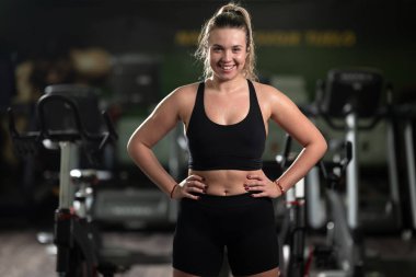 Formda bir kadın, yoğun bir egzersizden sonra spor salonunda kendine güvenen bir poz verir. Gücünü, bağlılığını ve gelişimini gösterir.