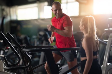 Spor salonunda birlikte çalışan bir çift, yan yana kondisyon çalışması yapıyorlar, birbirlerine güç, motivasyon ve takım çalışması ile destek oluyorlar.