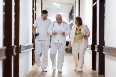 Hasta belgelerini inceleyip tedavi planlarını tartışırken beyaz üniformalı bir grup sağlık görevlisi hastane koridorunda yürüyorlar. 
