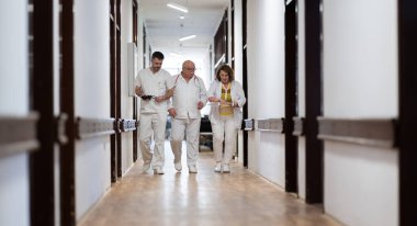 Hasta belgelerini inceleyip tedavi planlarını tartışırken beyaz üniformalı bir grup sağlık görevlisi hastane koridorunda yürüyorlar. 