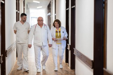 Hasta belgelerini inceleyip tedavi planlarını tartışırken beyaz üniformalı bir grup sağlık görevlisi hastane koridorunda yürüyorlar. 