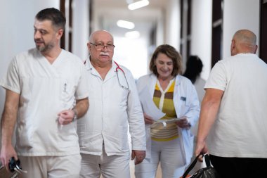 Hasta belgelerini inceleyip tedavi planlarını tartışırken beyaz üniformalı bir grup sağlık görevlisi hastane koridorunda yürüyorlar. 