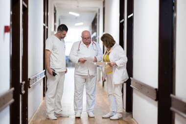 Hasta belgelerini inceleyip tedavi planlarını tartışırken beyaz üniformalı bir grup sağlık görevlisi hastane koridorunda yürüyorlar. 