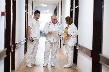 Hasta belgelerini inceleyip tedavi planlarını tartışırken beyaz üniformalı bir grup sağlık görevlisi hastane koridorunda yürüyorlar. 