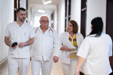 Hasta belgelerini inceleyip tedavi planlarını tartışırken beyaz üniformalı bir grup sağlık görevlisi hastane koridorunda yürüyorlar. 
