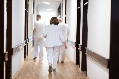 Hasta belgelerini inceleyip tedavi planlarını tartışırken beyaz üniformalı bir grup sağlık görevlisi hastane koridorunda yürüyorlar. 