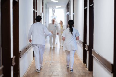 Doktorlar ve hemşireler de dahil olmak üzere sağlık personeli, yoğun bir hastane koridorunda acil müdahale ve kritik bir durumda ekip çalışmalarını sergileyerek acil müdahale ediyor.