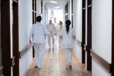 Hasta belgelerini inceleyip tedavi planlarını tartışırken beyaz üniformalı bir grup sağlık görevlisi hastane koridorunda yürüyorlar. 