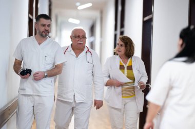 Hasta belgelerini inceleyip tedavi planlarını tartışırken beyaz üniformalı bir grup sağlık görevlisi hastane koridorunda yürüyorlar. 