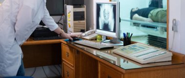 Beyaz laboratuvar önlüklü bir radyolog, bir hastanın kalça röntgenini incelerken bir çalışma odasında oturuyor.. 