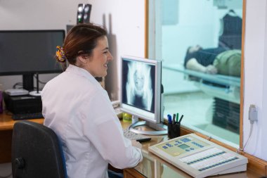 Beyaz laboratuvar önlüklü bir radyolog, bir hastanın kalça röntgenini incelerken bir çalışma odasında oturuyor.. 