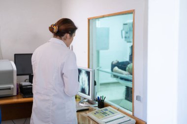 Beyaz laboratuvar önlüklü bir radyolog, bir hastanın kalça röntgenini incelerken bir çalışma odasında oturuyor.. 