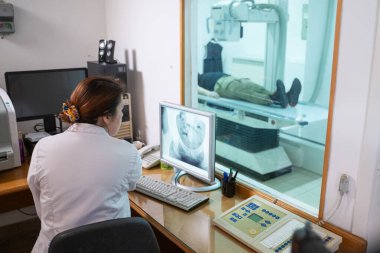 Beyaz laboratuvar önlüklü bir radyolog, bir hastanın kalça röntgenini incelerken bir çalışma odasında oturuyor.. 