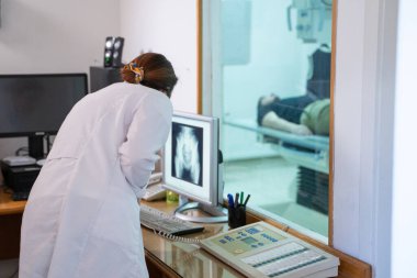Beyaz laboratuvar önlüklü bir radyolog, bir hastanın kalça röntgenini incelerken bir çalışma odasında oturuyor.. 