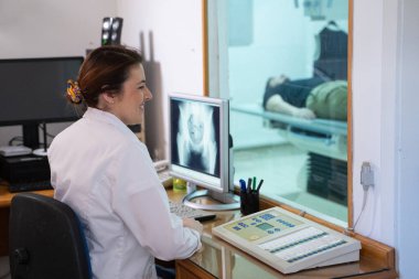 Beyaz laboratuvar önlüklü bir radyolog, bir hastanın kalça röntgenini incelerken bir çalışma odasında oturuyor.. 