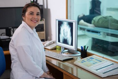 Beyaz laboratuvar önlüklü bir radyolog, bir hastanın kalça röntgenini incelerken bir çalışma odasında oturuyor.. 