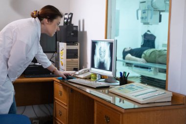 Beyaz laboratuvar önlüklü bir radyolog, bir hastanın kalça röntgenini incelerken bir çalışma odasında oturuyor.. 