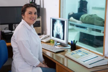 Beyaz laboratuvar önlüklü bir radyolog, bir hastanın kalça röntgenini incelerken bir çalışma odasında oturuyor.. 
