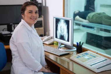 Beyaz laboratuvar önlüklü bir radyolog, bir hastanın kalça röntgenini incelerken bir çalışma odasında oturuyor.. 