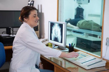 Beyaz laboratuvar önlüklü bir radyolog, bir hastanın kalça röntgenini incelerken bir çalışma odasında oturuyor.. 