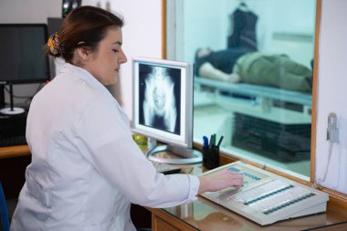 Beyaz laboratuvar önlüklü bir radyolog, bir hastanın kalça röntgenini incelerken bir çalışma odasında oturuyor.. 