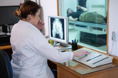 Beyaz laboratuvar önlüklü bir radyolog, bir hastanın kalça röntgenini incelerken bir çalışma odasında oturuyor.. 
