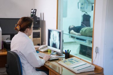 Beyaz laboratuvar önlüklü bir radyolog, bir hastanın kalça röntgenini incelerken bir çalışma odasında oturuyor.. 