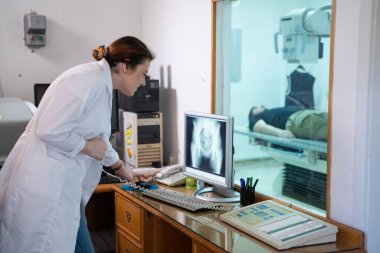 Beyaz laboratuvar önlüklü bir radyolog, bir hastanın kalça röntgenini incelerken bir çalışma odasında oturuyor.. 