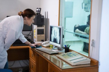 Beyaz laboratuvar önlüklü bir radyolog, bir hastanın kalça röntgenini incelerken bir çalışma odasında oturuyor.. 