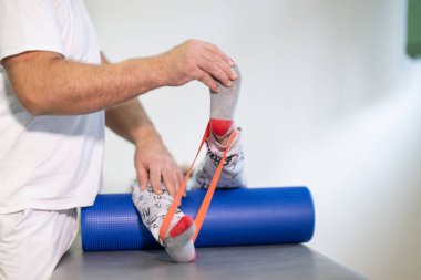 Terapist, fizik tedavi seansında direnç bandı kullanarak bacak esnetmeye yardım ediyor..