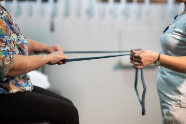 Kıdemli kadın gülümseyen bir terapistin yardımıyla fiziksel egzersiz yapıyor. Yaşlıların rehabilitasyonu ve hareket düzelmesi kavramı.