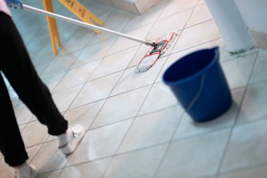 Hastane koridorunda elinde paspas ve kovayla duran kadın hademe temizliği ve hijyeni simgeliyor..