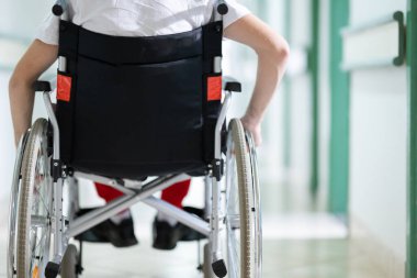 Genç bir çocuk hastane koridorunda tekerlekli sandalyede otururken gülümsüyor. Rehabilitasyon ve pozitiflik kavramı