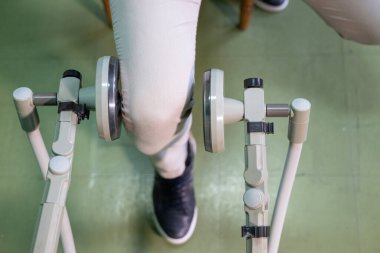 Rehabilitasyon makinesini bacak terapisi için kullanan, kas eğitimi ve hareket kabiliyetine odaklanan bir insanın alt görünümü.