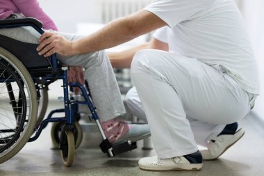 Kıdemli kadın gülümseyen bir terapistin yardımıyla fiziksel egzersiz yapıyor. Yaşlıların rehabilitasyonu ve hareket düzelmesi kavramı.