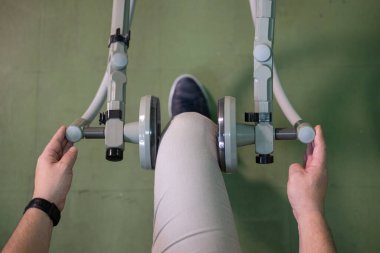 Rehabilitasyon makinesini bacak terapisi için kullanan, kas eğitimi ve hareket kabiliyetine odaklanan bir insanın alt görünümü.