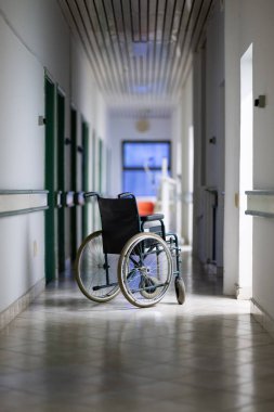 Parlak bir hastane koridorunda sahipsiz tekerlekli sandalye var. Erişilebilirlik ve hasta taşımacılığı kavramı.