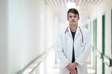 Genç bir erkek doktor steteskopla hastane koridorunda güvenle duruyor. Tıbbi profesyonellik kavramı.