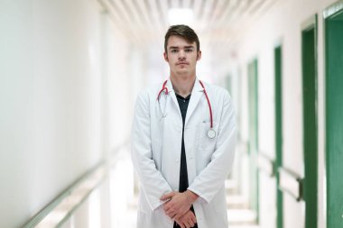 Genç bir erkek doktor steteskopla hastane koridorunda güvenle duruyor. Tıbbi profesyonellik kavramı.