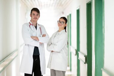 Beyaz önlüklü erkek ve kadın doktorlar hastane koridorunda güven içinde poz veriyorlar. Takım çalışması ve sağlık hizmeti kavramı.