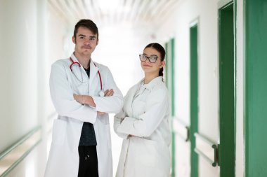 Beyaz önlüklü erkek ve kadın doktorlar hastane koridorunda güven içinde poz veriyorlar. Takım çalışması ve sağlık hizmeti kavramı.