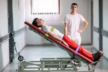 Erkek terapist, klinik koridordaki bir rehabilitasyon sırasında ayakta duran bir çerçeveyle hastaya yardım ediyor. Fiziksel iyileşme desteği kavramı.