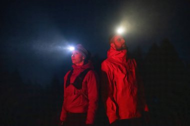 Fenerlerle donatılmış çift, gece havasını kesen ışık huzmeleriyle zifiri karanlıkta bir ormanı keşfediyor..