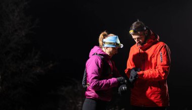 Gece yürüyüşçüleri, düşük ışık koşulları altında navigasyon ve takım çalışmasını vurgulayan far ışığı altında bir cihazı incelerler..