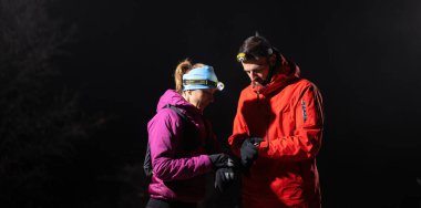 Gece yürüyüşçüleri, düşük ışık koşulları altında navigasyon ve takım çalışmasını vurgulayan far ışığı altında bir cihazı incelerler..