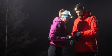 Gece yürüyüşçüleri, düşük ışık koşulları altında navigasyon ve takım çalışmasını vurgulayan far ışığı altında bir cihazı incelerler..